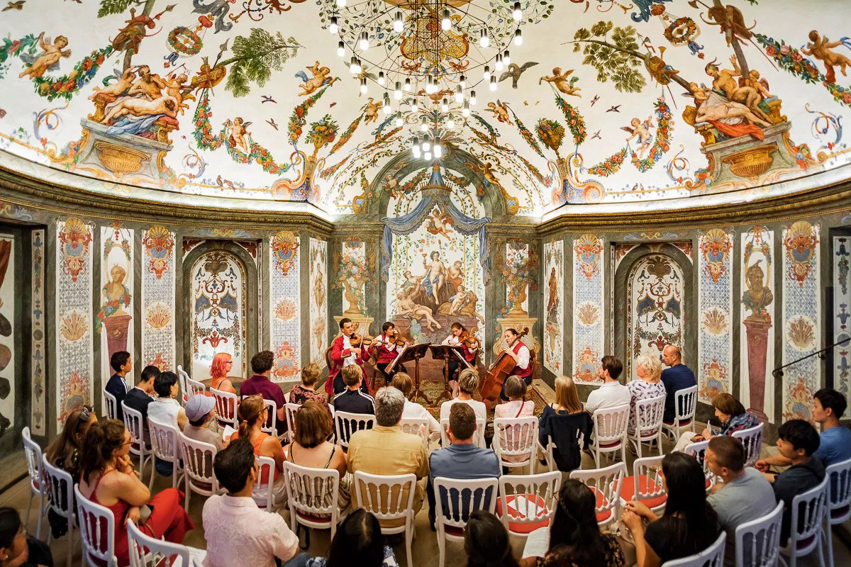 The Sala Terrena during a concert: the quartet in red coats before the frescoed apse, the whole audience on white chairs beneath the painted vault.