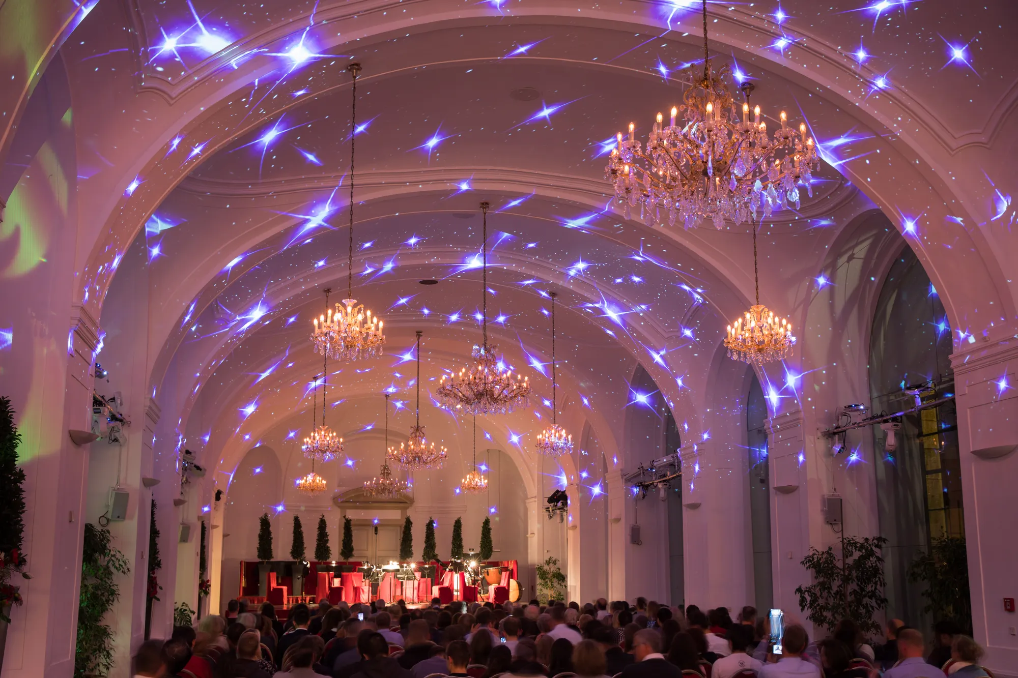 The Orangery hall full for a concert, its vaulted ceiling lit and the chandeliers down the length of the room.